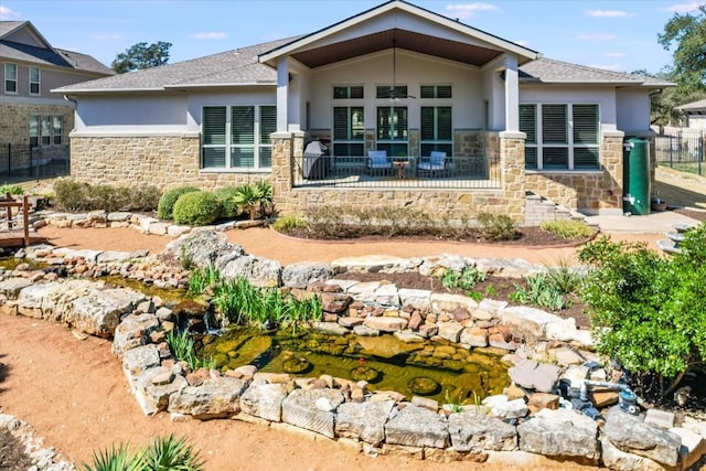 back of property with stone siding, fence, and stucco siding