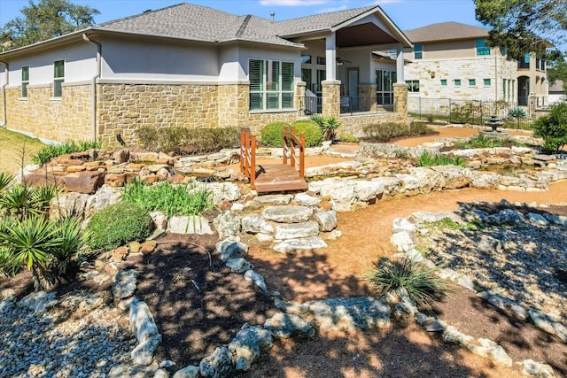 back of house with stone siding, a shingled roof, fence, and stucco siding