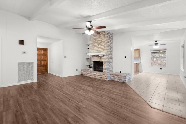 unfurnished living room featuring a textured ceiling, lofted ceiling with beams, a fireplace, wood finished floors, and visible vents