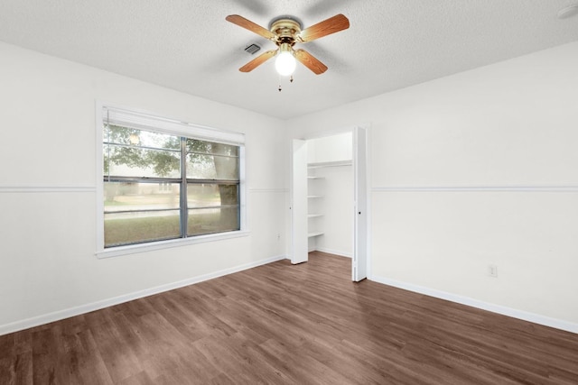 empty room with dark wood-style floors, a textured ceiling, visible vents, and baseboards