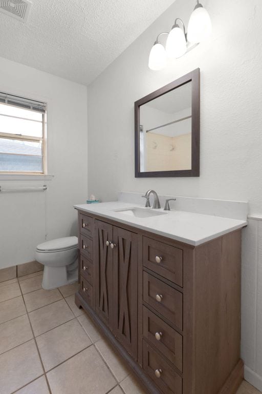 bathroom with visible vents, toilet, vanity, a textured ceiling, and tile patterned floors