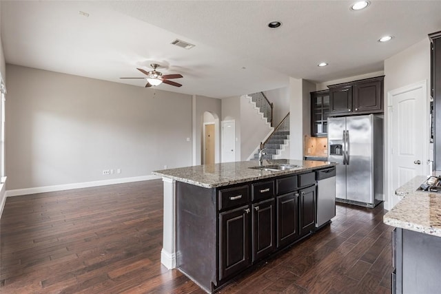 201 Seminole Canyon Dr, Georgetown, TX 78628 - kitchen featuring appliances with stainless steel finishes, arched walkways, a ceiling fan, a center island with sink, and dark wood-style floors