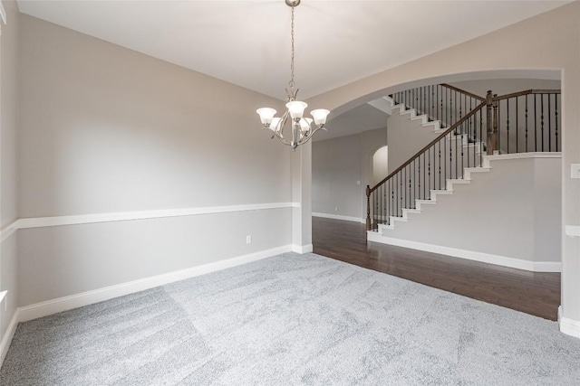 carpeted empty room with arched walkways, lofted ceiling, baseboards, stairway, and an inviting chandelier