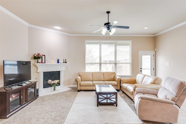 living area with light colored carpet, a ceiling fan, baseboards, ornamental molding, and a glass covered fireplace