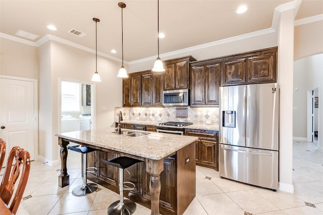 kitchen featuring a kitchen island with sink, stainless steel appliances, a sink, a kitchen breakfast bar, and independent washer and dryer