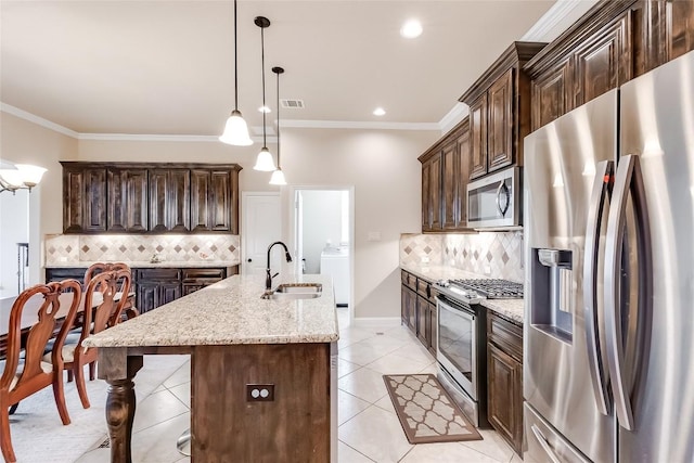 kitchen featuring pendant lighting, a center island with sink, appliances with stainless steel finishes, a sink, and light stone countertops