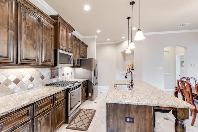 kitchen featuring arched walkways, stainless steel appliances, a sink, hanging light fixtures, and a center island with sink