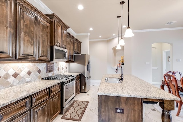 1312 Mustang Brook Ln, Leander, TX 78641 - kitchen featuring stainless steel appliances, arched walkways, a kitchen island with sink, tasteful backsplash, and dark brown cabinets