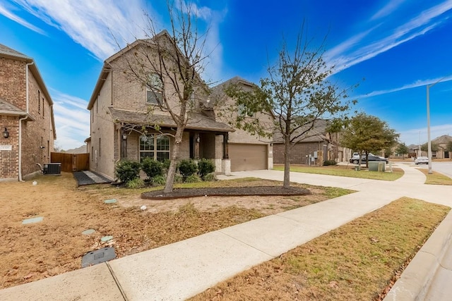 view of front of home with an attached garage, central AC, brick siding, concrete driveway, and a front yard