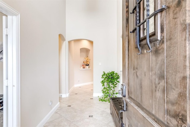 hall featuring arched walkways, baseboards, and light tile patterned floors