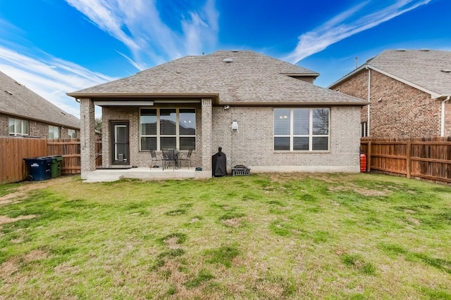 back of property featuring a yard, a fenced backyard, roof with shingles, and brick siding