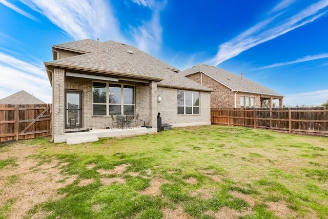 back of property featuring a patio, a fenced backyard, roof with shingles, a yard, and brick siding