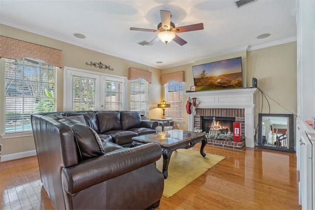 living room featuring a wealth of natural light, light wood-type flooring, a brick fireplace, and crown molding