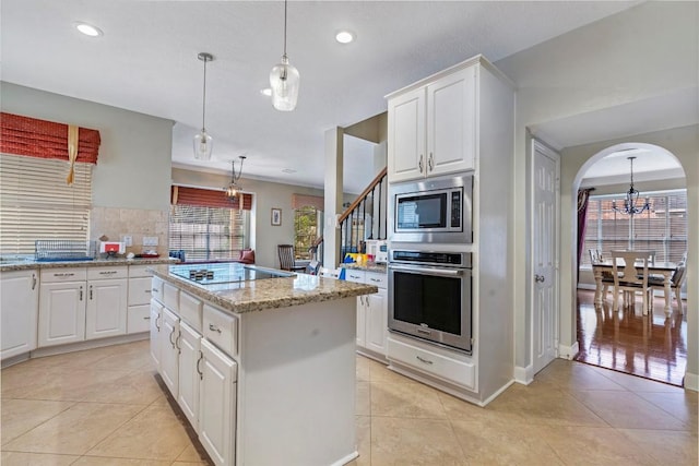 kitchen with arched walkways, appliances with stainless steel finishes, a center island, decorative light fixtures, and white cabinetry