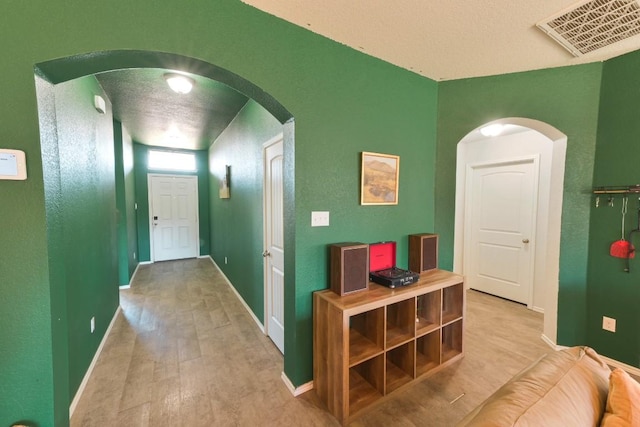 hall featuring arched walkways, light wood finished floors, visible vents, and baseboards