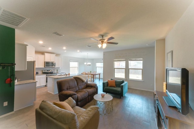 living area with light wood-type flooring, visible vents, and ceiling fan with notable chandelier