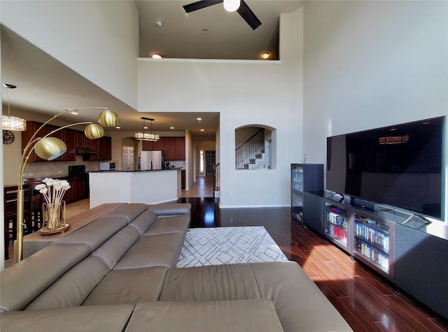 living room with arched walkways, dark wood-style floors, ceiling fan, stairway, and a high ceiling