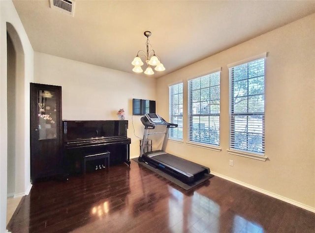 exercise area with arched walkways, visible vents, an inviting chandelier, dark wood-type flooring, and baseboards