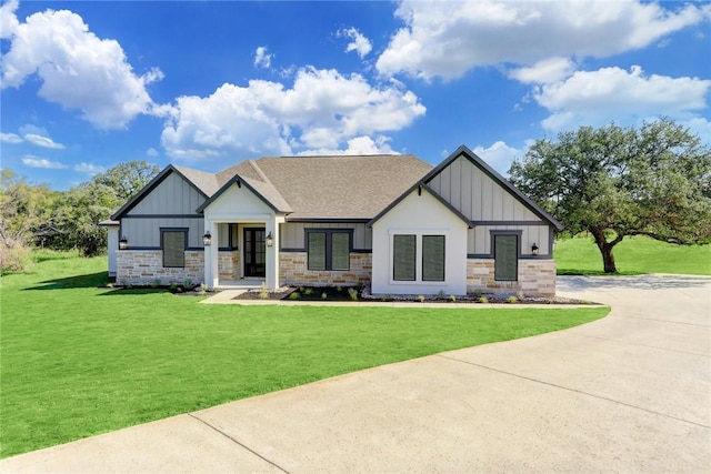 view of front of property with board and batten siding, a front yard, concrete driveway, and stone siding