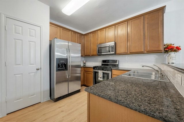 kitchen with stainless steel appliances, backsplash, light wood-style floors, brown cabinetry, and a sink