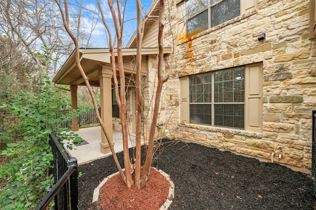 view of side of property featuring stone siding and fence