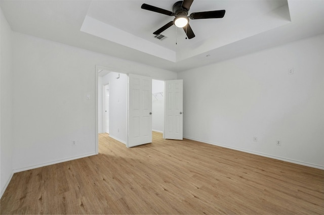 unfurnished bedroom with a tray ceiling, visible vents, ceiling fan, light wood-type flooring, and baseboards