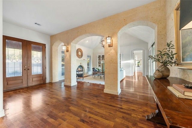 entrance foyer with visible vents, dark wood finished floors, a lit fireplace, vaulted ceiling, and french doors