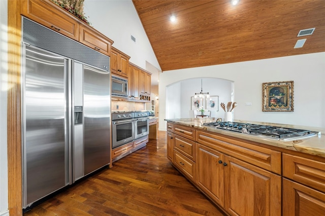 kitchen featuring visible vents, arched walkways, brown cabinetry, built in appliances, and hanging light fixtures