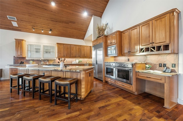 kitchen featuring built in appliances, a breakfast bar, visible vents, light countertops, and an island with sink