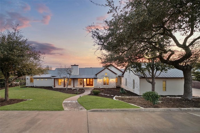 view of front of house with metal roof, stone siding, a yard, a standing seam roof, and a chimney