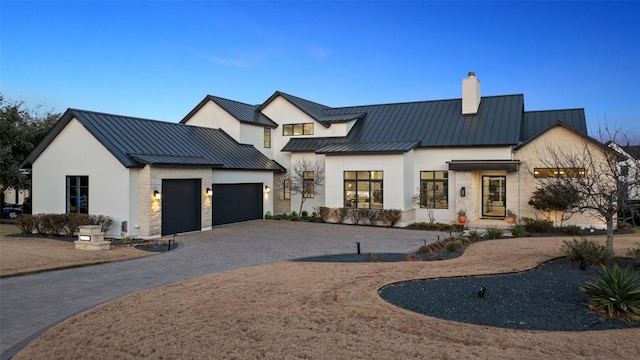 modern farmhouse with decorative driveway, a chimney, a standing seam roof, metal roof, and stone siding