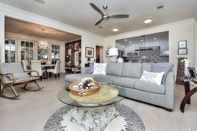 living room with ceiling fan with notable chandelier, visible vents, crown molding, and wood finished floors