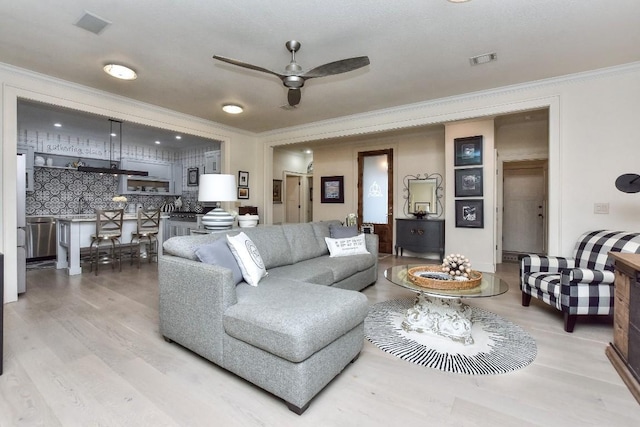 living area with ceiling fan, ornamental molding, wood finished floors, and visible vents