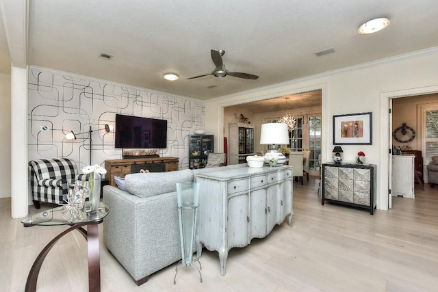 living room with ornamental molding, visible vents, light wood finished floors, and a ceiling fan