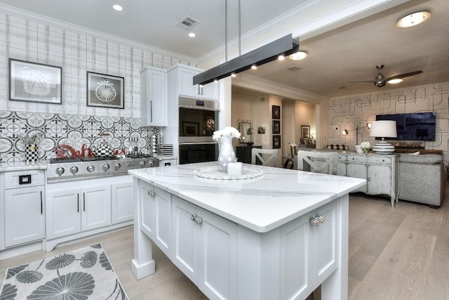 kitchen with wallpapered walls, white cabinets, ornamental molding, appliances with stainless steel finishes, and open floor plan