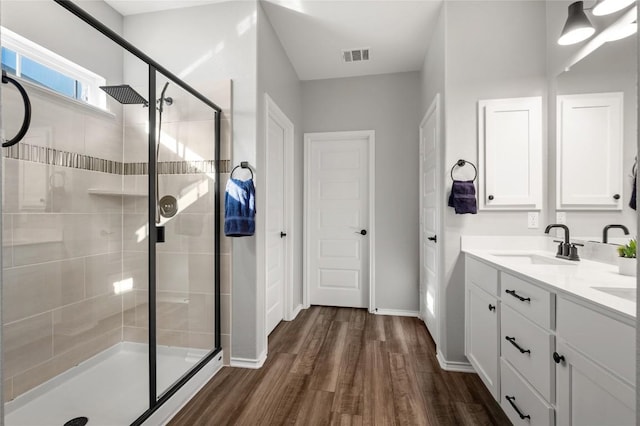 full bath with visible vents, a sink, a shower stall, wood finished floors, and baseboards