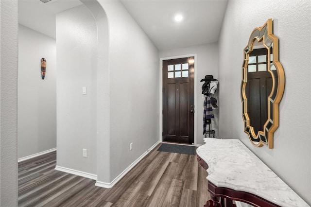 entrance foyer featuring dark wood-style floors, arched walkways, and baseboards