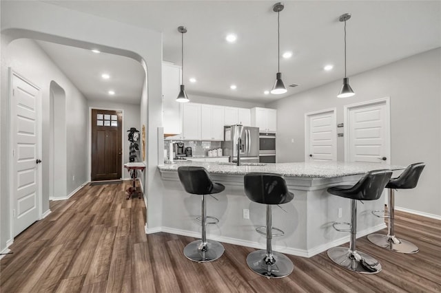 kitchen featuring arched walkways, hanging light fixtures, appliances with stainless steel finishes, white cabinets, and light stone countertops