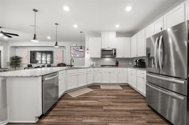 kitchen with decorative light fixtures, stainless steel appliances, white cabinets, a sink, and light stone countertops