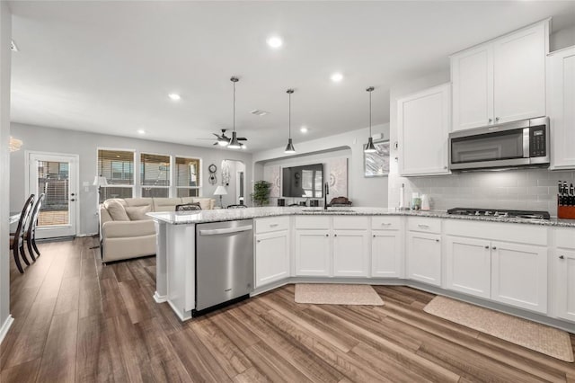 kitchen featuring a sink, white cabinets, open floor plan, hanging light fixtures, and appliances with stainless steel finishes