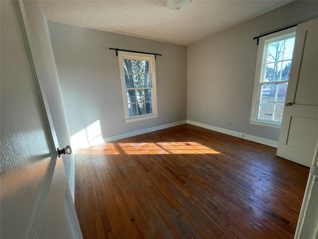 spare room featuring dark wood-style floors, a textured ceiling, and baseboards