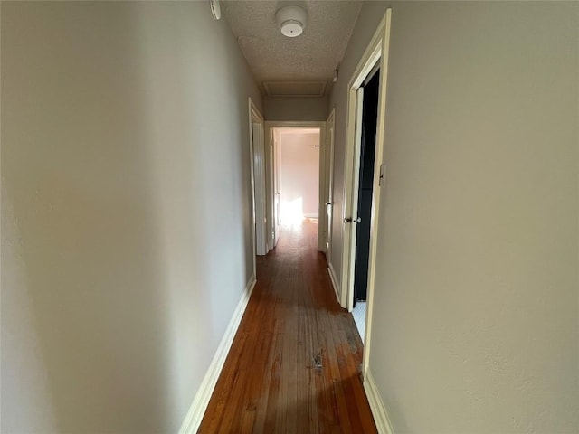 corridor featuring dark wood-type flooring, attic access, a textured ceiling, and baseboards