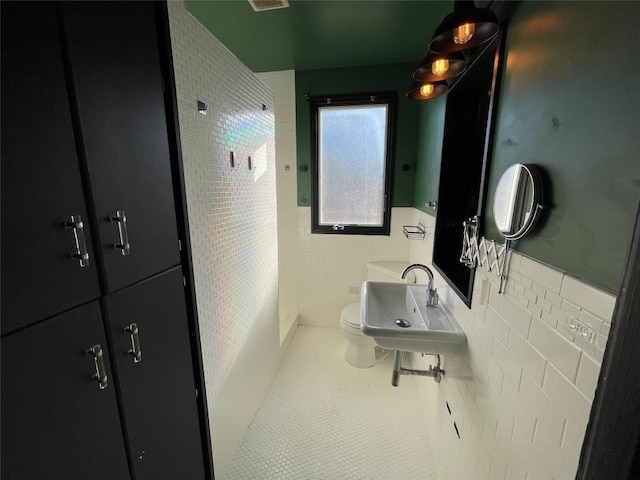 full bath with a walk in shower, toilet, a sink, tile walls, and tile patterned floors