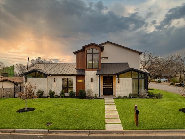 view of front of house with a standing seam roof, brick siding, a lawn, and metal roof