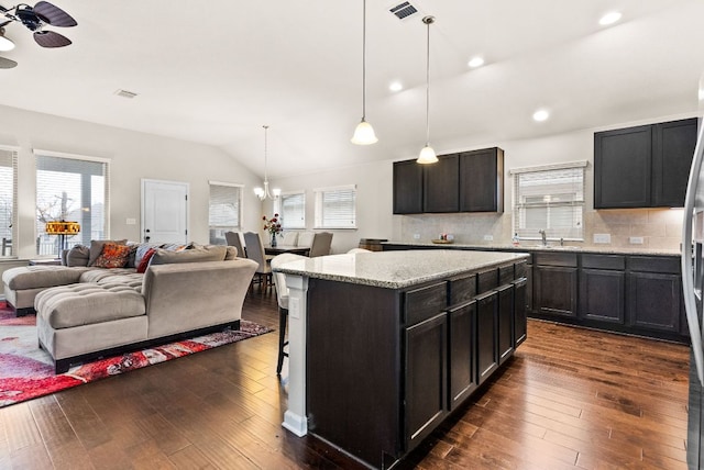 kitchen featuring a kitchen island, open floor plan, dark wood-style flooring, light stone countertops, and pendant lighting