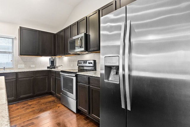 kitchen with dark wood finished floors, vaulted ceiling, stainless steel appliances, and decorative backsplash