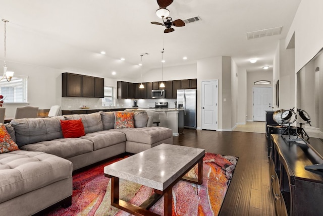 living room featuring dark wood-style floors, visible vents, vaulted ceiling, and ceiling fan with notable chandelier