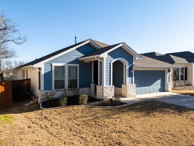 view of front of house featuring stone siding, concrete driveway, fence, and an attached garage