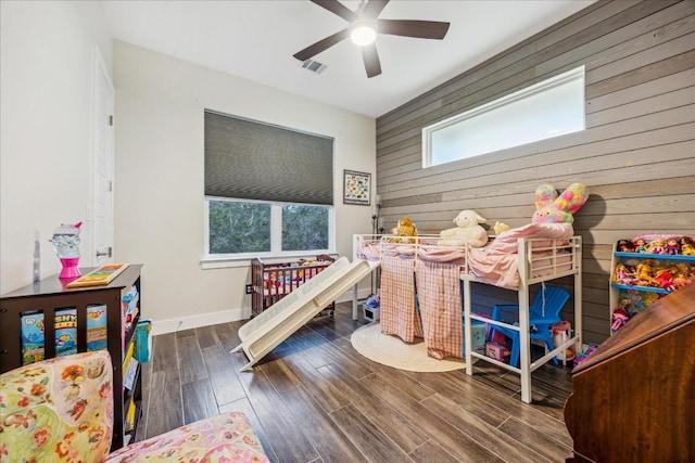 bedroom featuring a ceiling fan, baseboards, visible vents, wooden walls, and wood finished floors