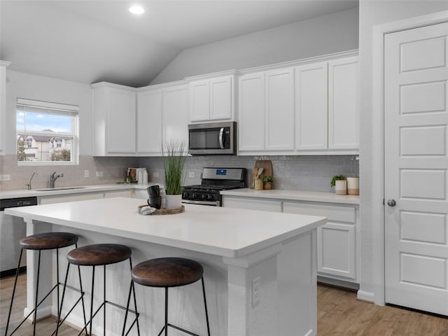 kitchen featuring a kitchen island, a sink, appliances with stainless steel finishes, a kitchen bar, and light wood-type flooring